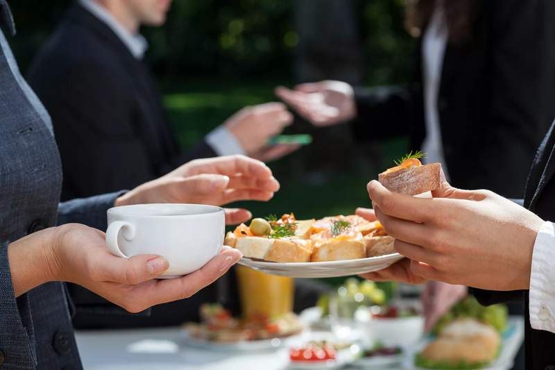 People at an outdoor gathering engaging in conversation while holding food and beverages.