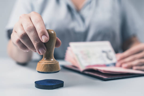 Person holds a stamp above ink pad with a passport open in the other hand, symbolizing visa application.