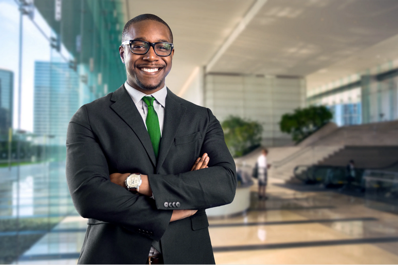 A man in a suit standing confidently with arms crossed in a modern glass office building.